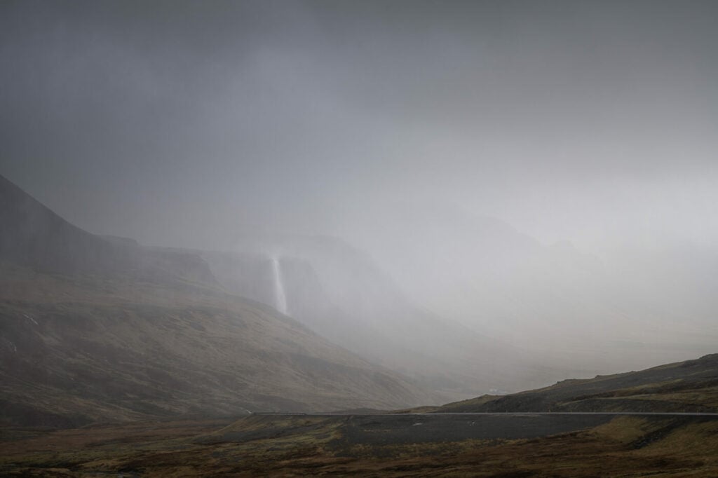 A waterfall barely visible behind a layer of rain on a dark and gloomy day.