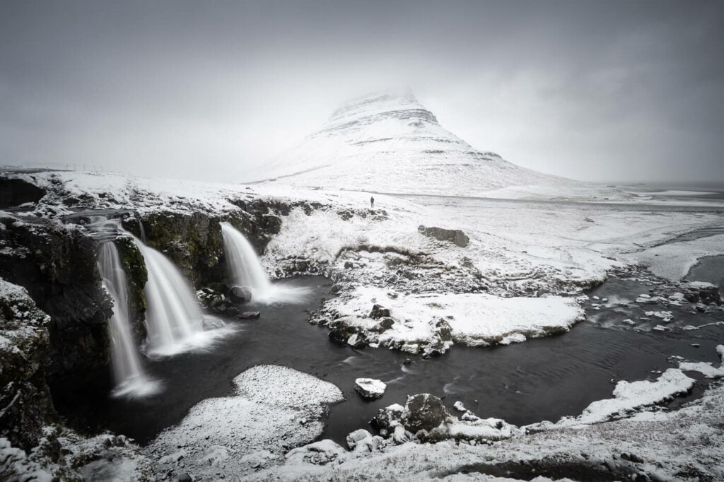 Kirkjufellsfoss and mount kirkjufell under the snow on a cloudy day