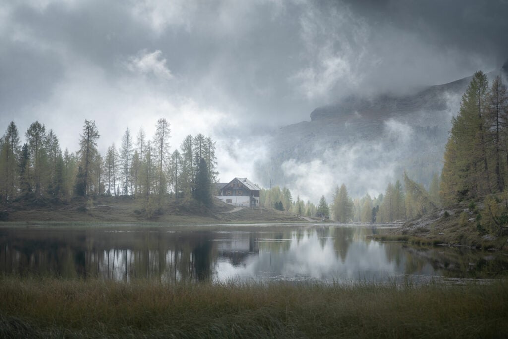 mountain hut reflecting in a lake under a cloudy and dull sky