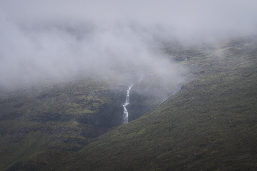 A lone waterfall seemingly popping out of a cloudy sky in a flat and dull environment.