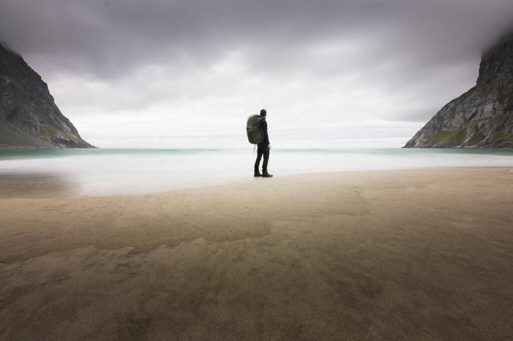 hiker with a backpack on a beach in a long exposure photo looking at the horizon