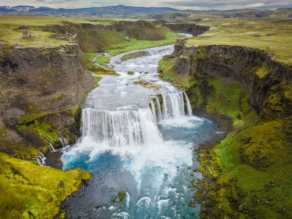 Drone view of a waterfall in the highlands of Iceland, with a canyon in the background.