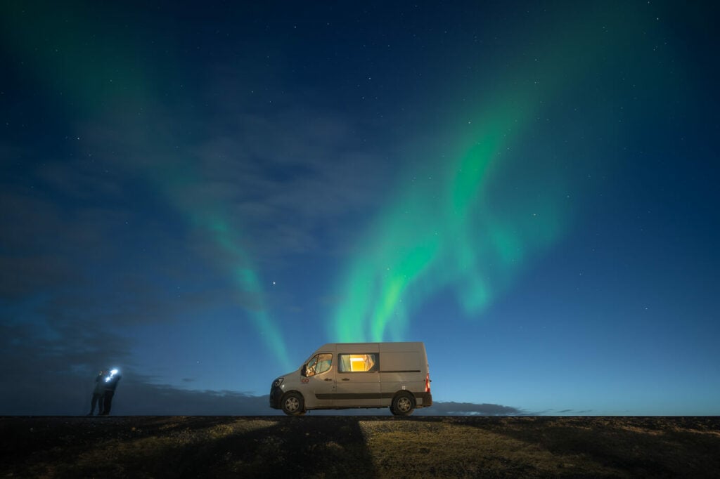 Van and people under the northern lights in Iceland