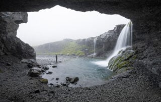 Hiker looking at skutafoss, a waterfall view from within a cave in East Iceland