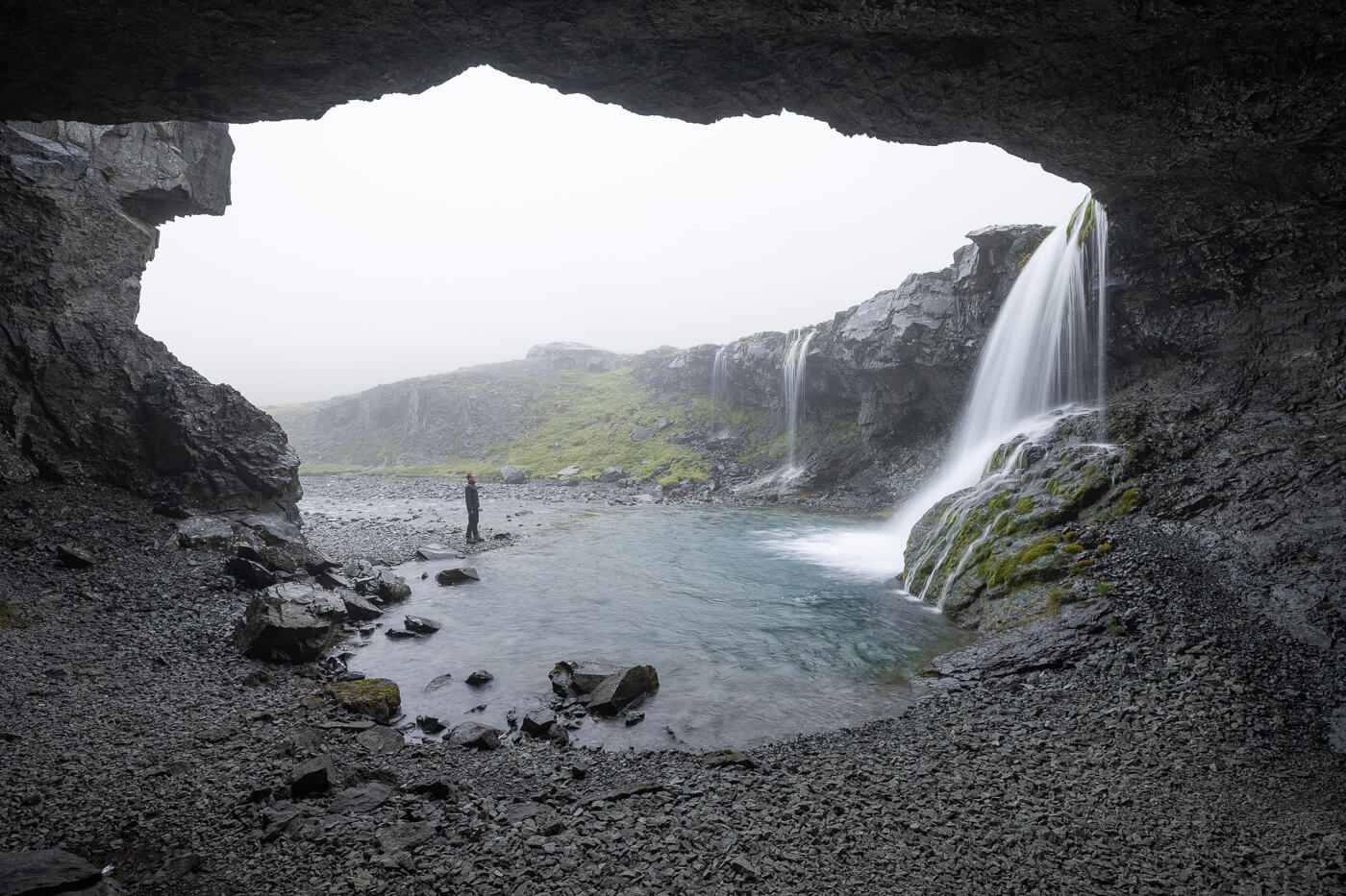 Hiker looking at skutafoss, a waterfall view from within a cave in East Iceland