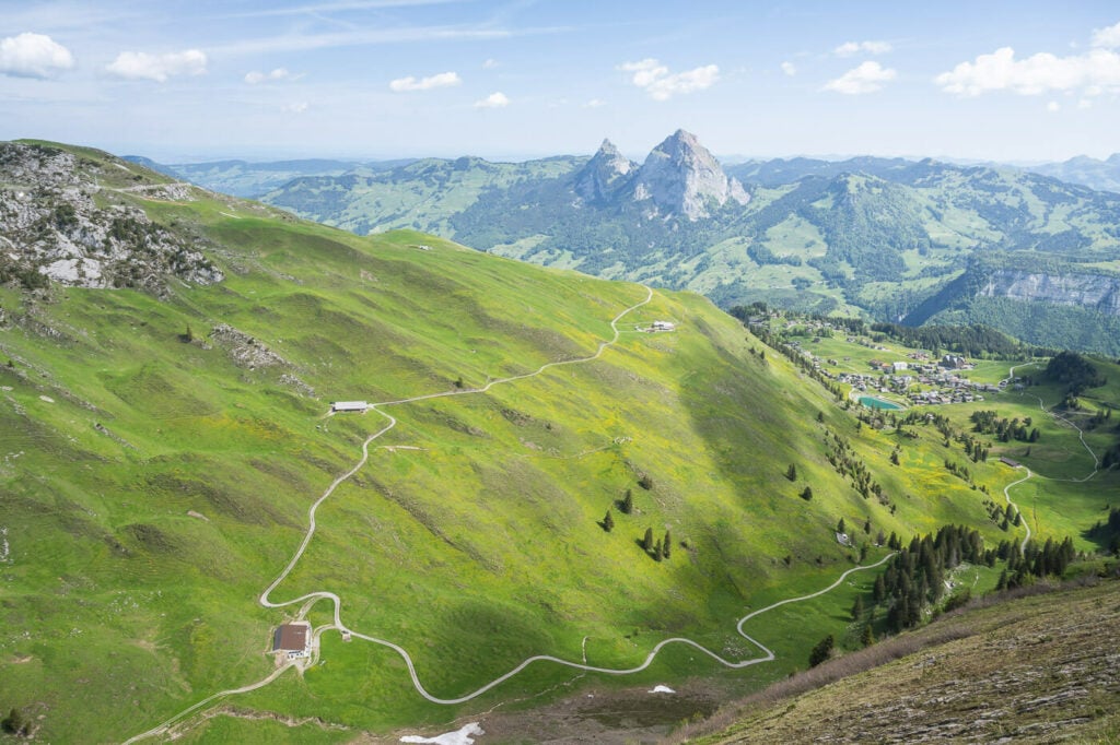 Panoramic image of green fields in the mountains of Switzerland with the small village of Stoos in the distance.