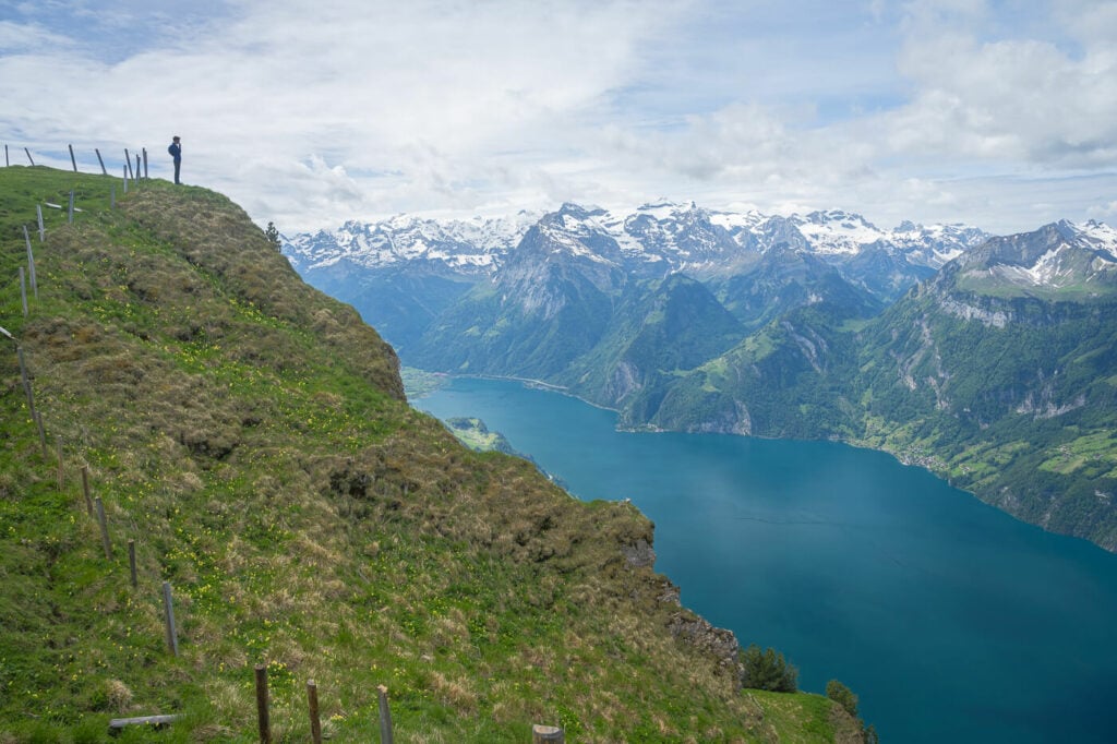 Hiker standing on top of a cliff looking at the landscape along the Stoos ridge trail