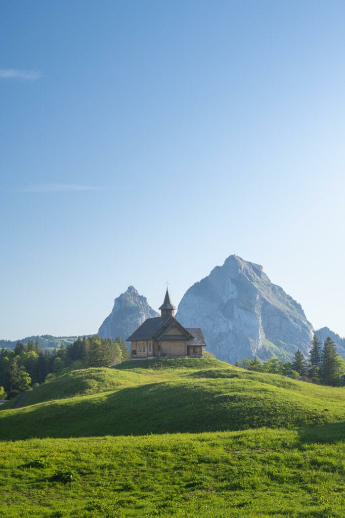 Stoos mountain Church on a sunny day with mountains in the background under a cloudless sky.