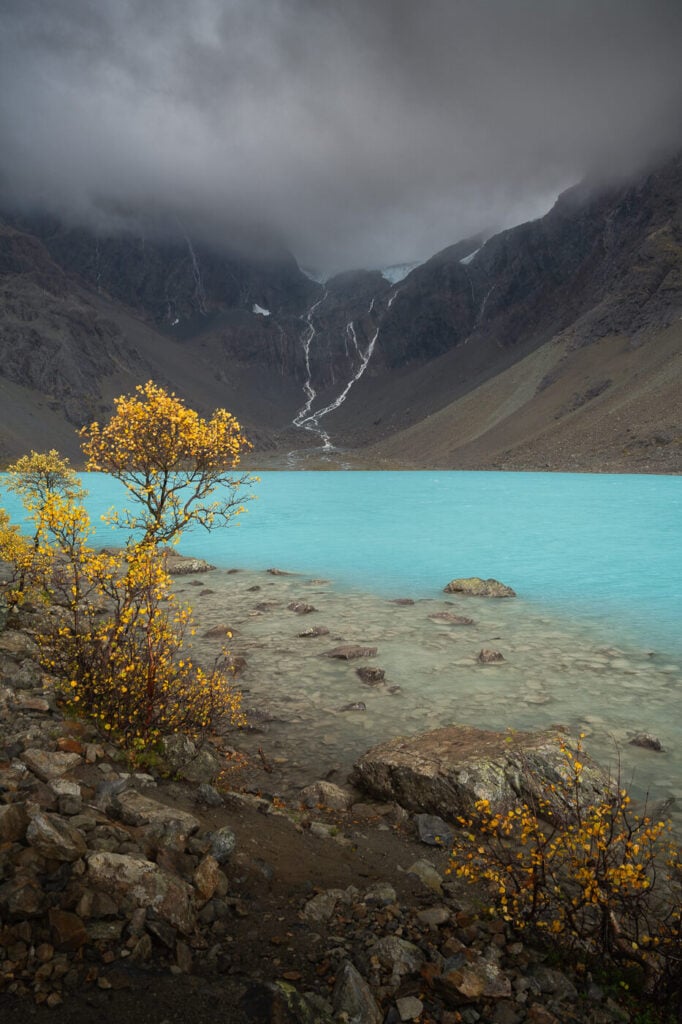 Blåisvatnet on a dark and cloudy autumn day, with waterfalls falling from a glacier in the distance.