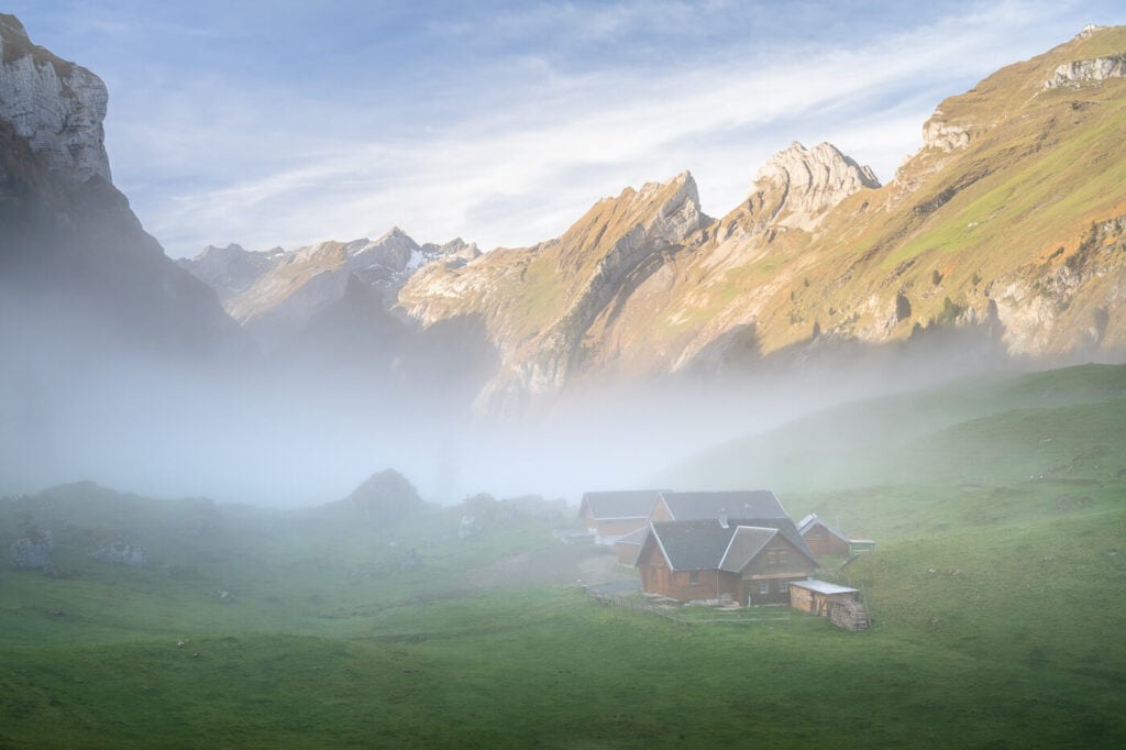 Alpesten huts above Seelpsee covered in fog, with mountains emerging in the background