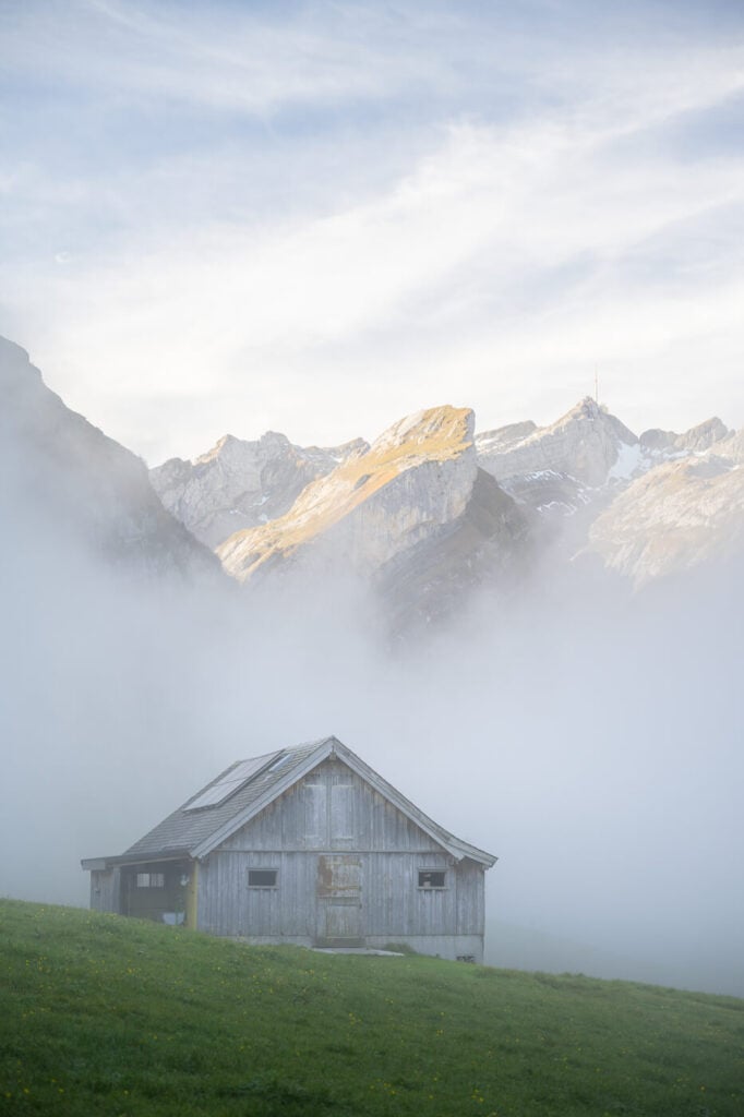 Barn in the fog with mountain tops visible above it.