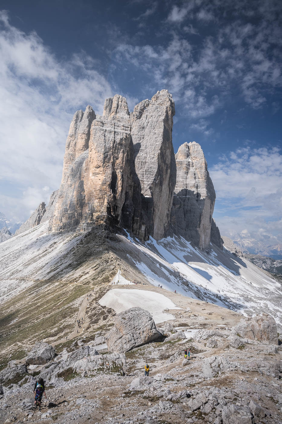 View of le tre cime di Lavaredo with several hikers around them, under a blue sky from Forcella Lavaredo