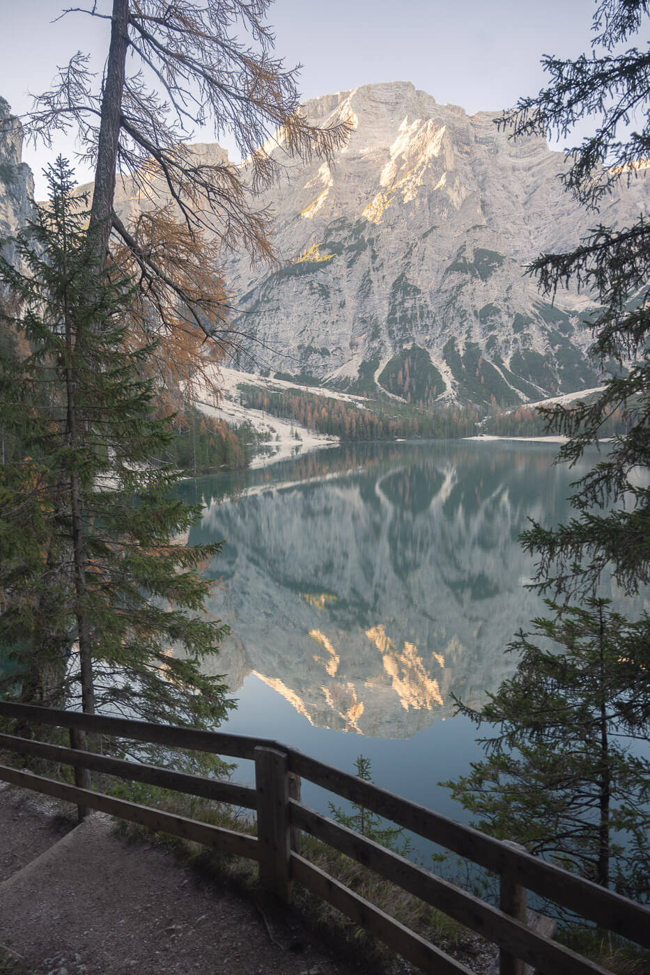 Lago di braies loop hike trail with fences protecting from a cliff, and view of the mountains in the background.