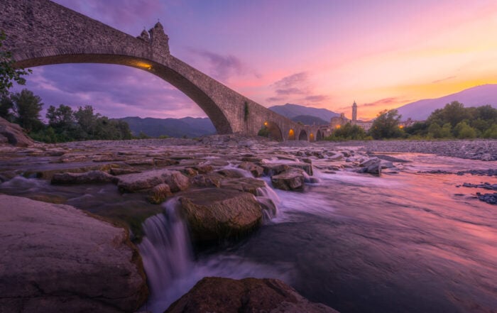 View of the Ponte Gobbo in Bobbio at sunset, with Colorful skies