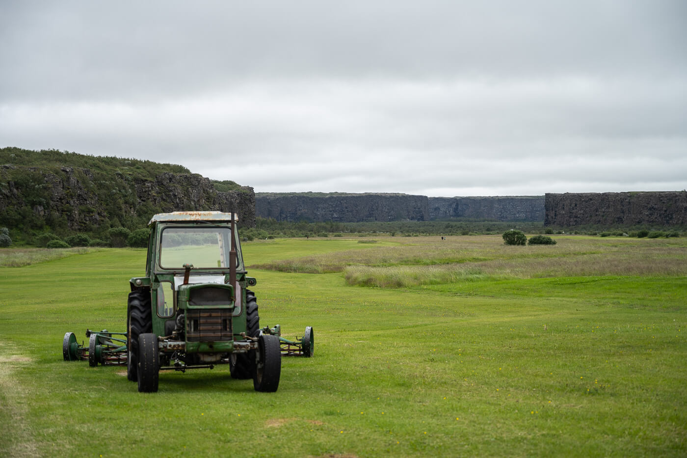 Tractor on a grass filed with the Ásbyrgi canyon in the background