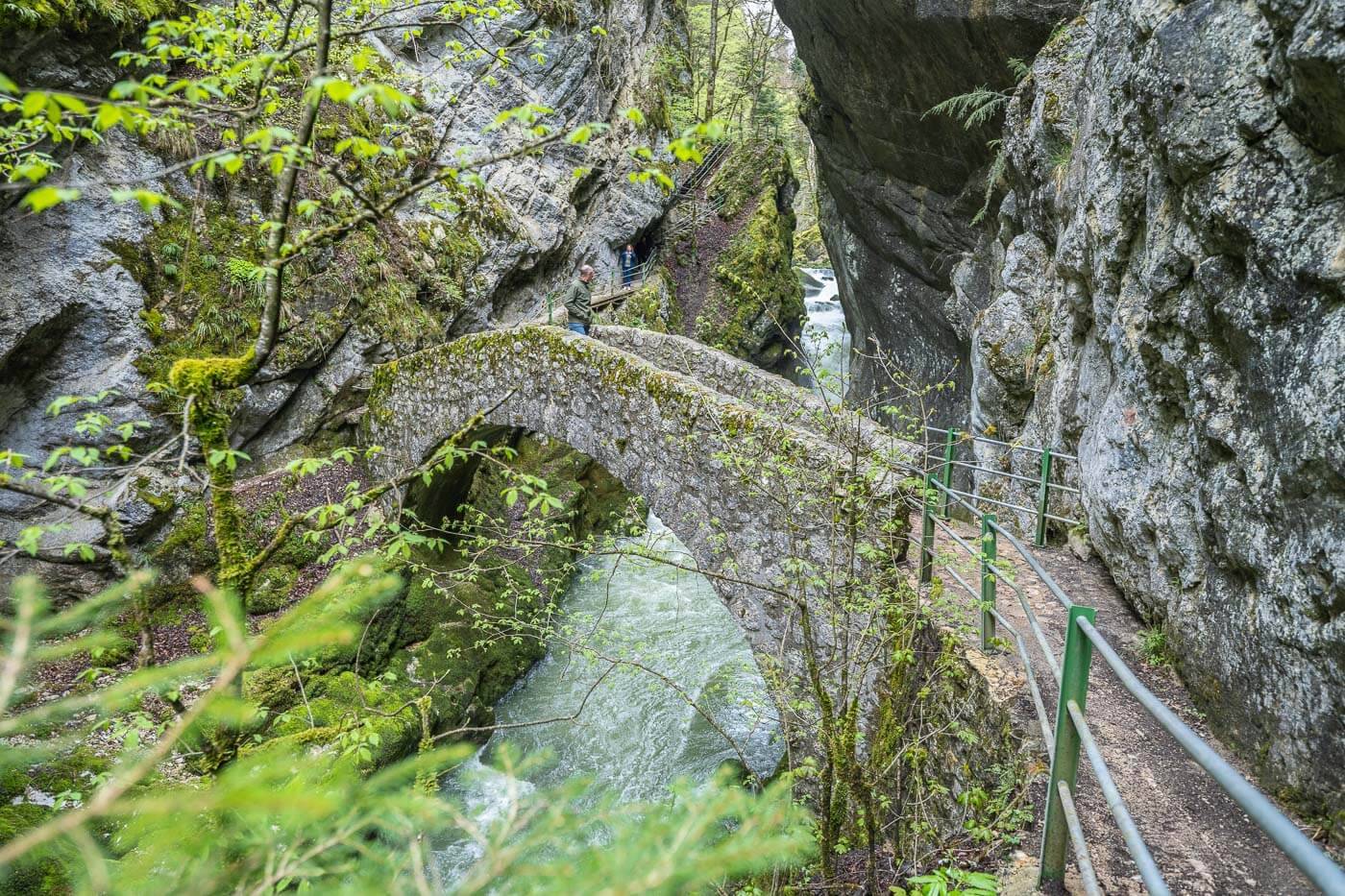 Hiker watching the river from a stone bridge above it.
