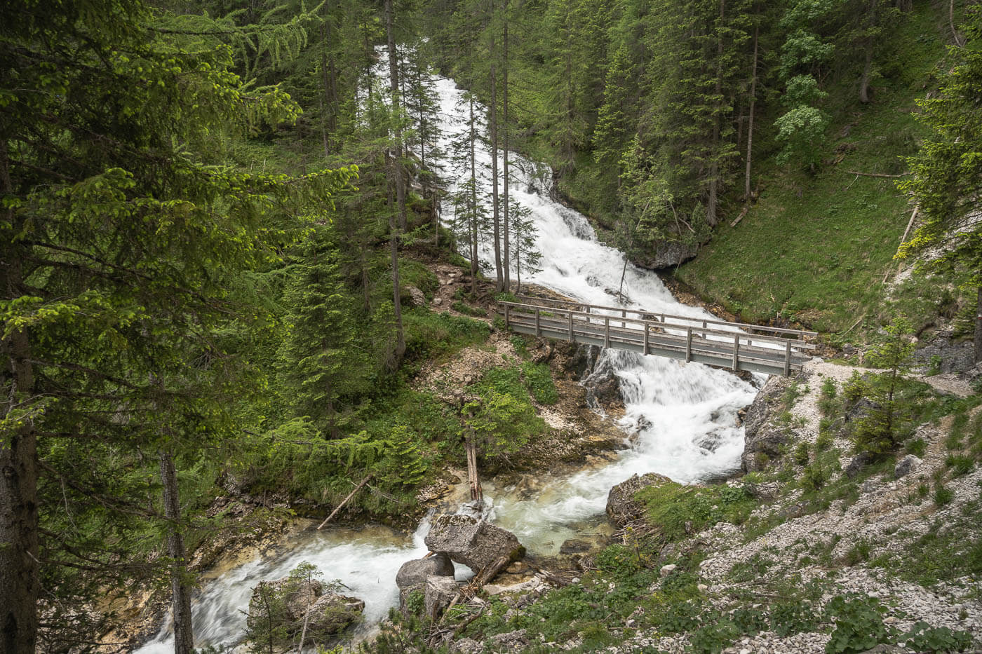 View of Ponte sulla Cascata del Torrente Boite on the Fanes waterfalls hiking trail, a waterfall in the forest in the Dolomites.