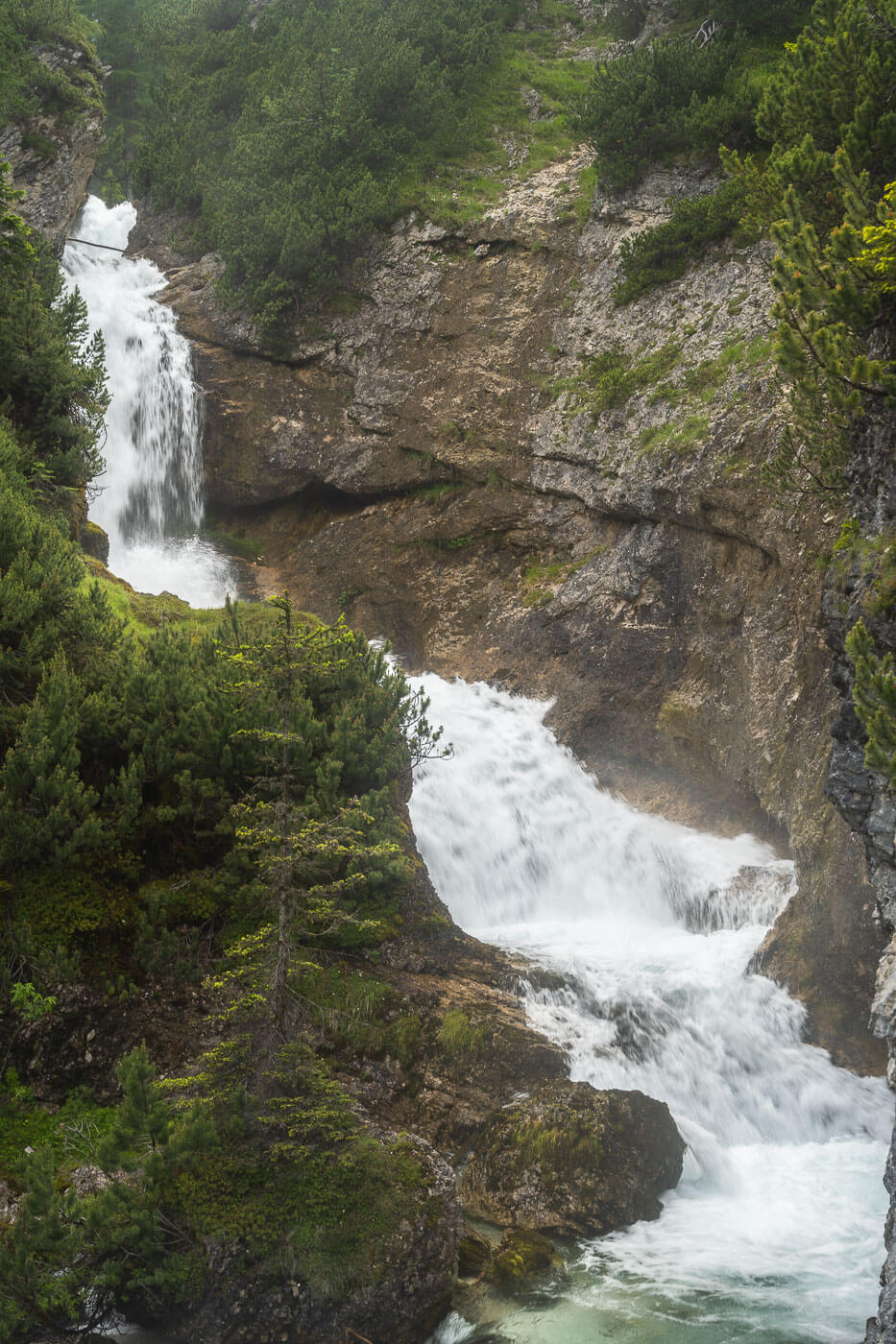 View of one of the many Fanes Waterfalls in the Dolomites, with a waterfall nestled in a small gorge in the forest.