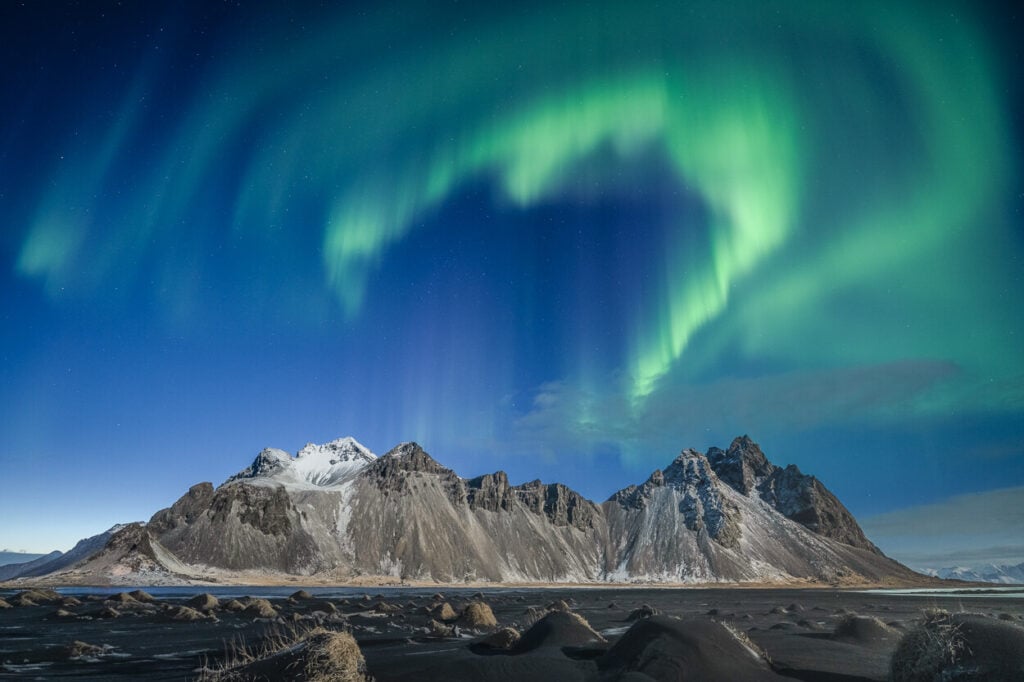 Photo of Northern lights in Iceland above Vestrahorn, with the aurora dancing above the snow-dusted moutain.
