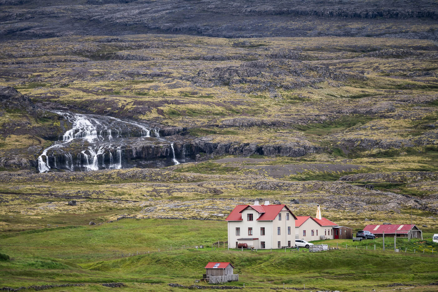 Telephoto landscape photo of. a farm with a waterfall in the background in the Westfjords of Iceland.