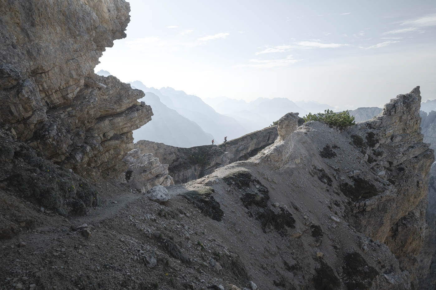 Two hikers on a ridge walking in the dolomites with the sun backlighting the scene.,