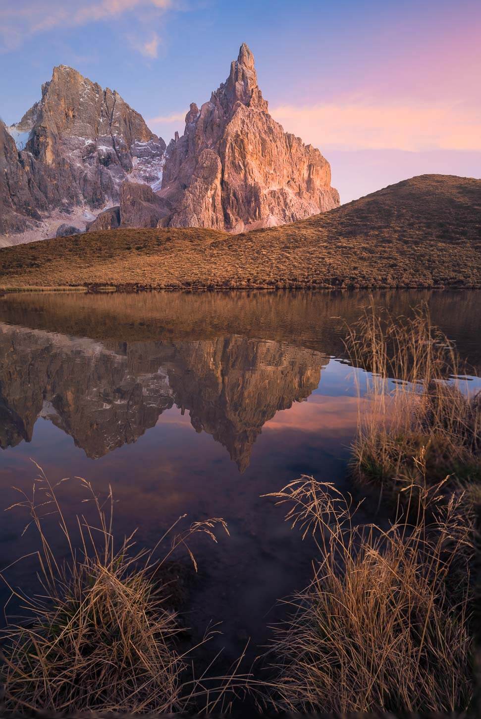 View of Cimon della Pala reflecting in a lake catching the Alpenglow after sunset at one of the classic photo spots in the Dolomites.
