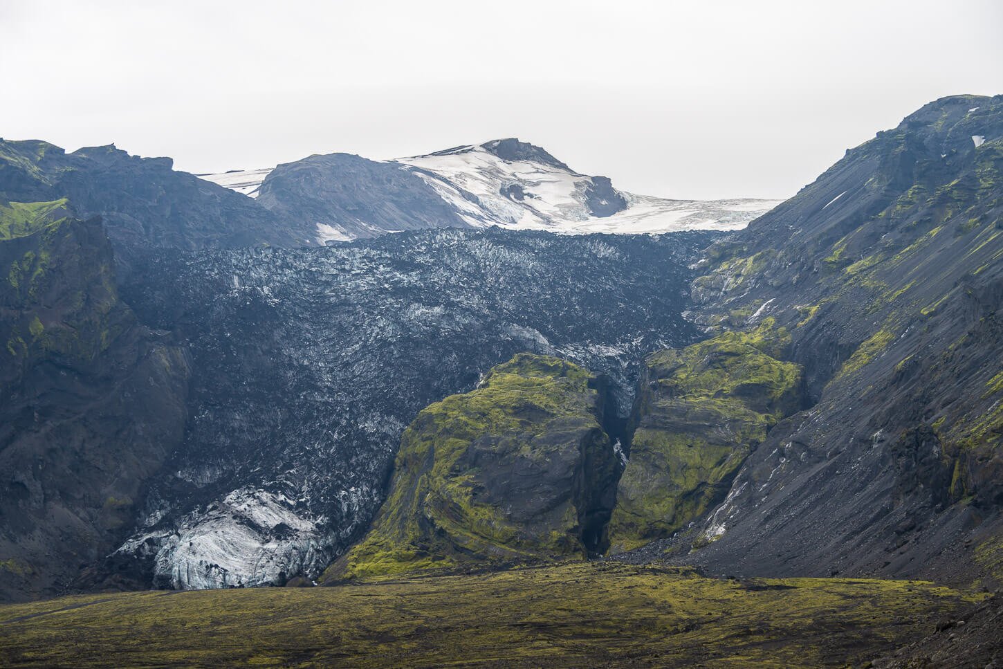 View of the Gígjökull glacier tongue covered in black ashes on a cloudy day