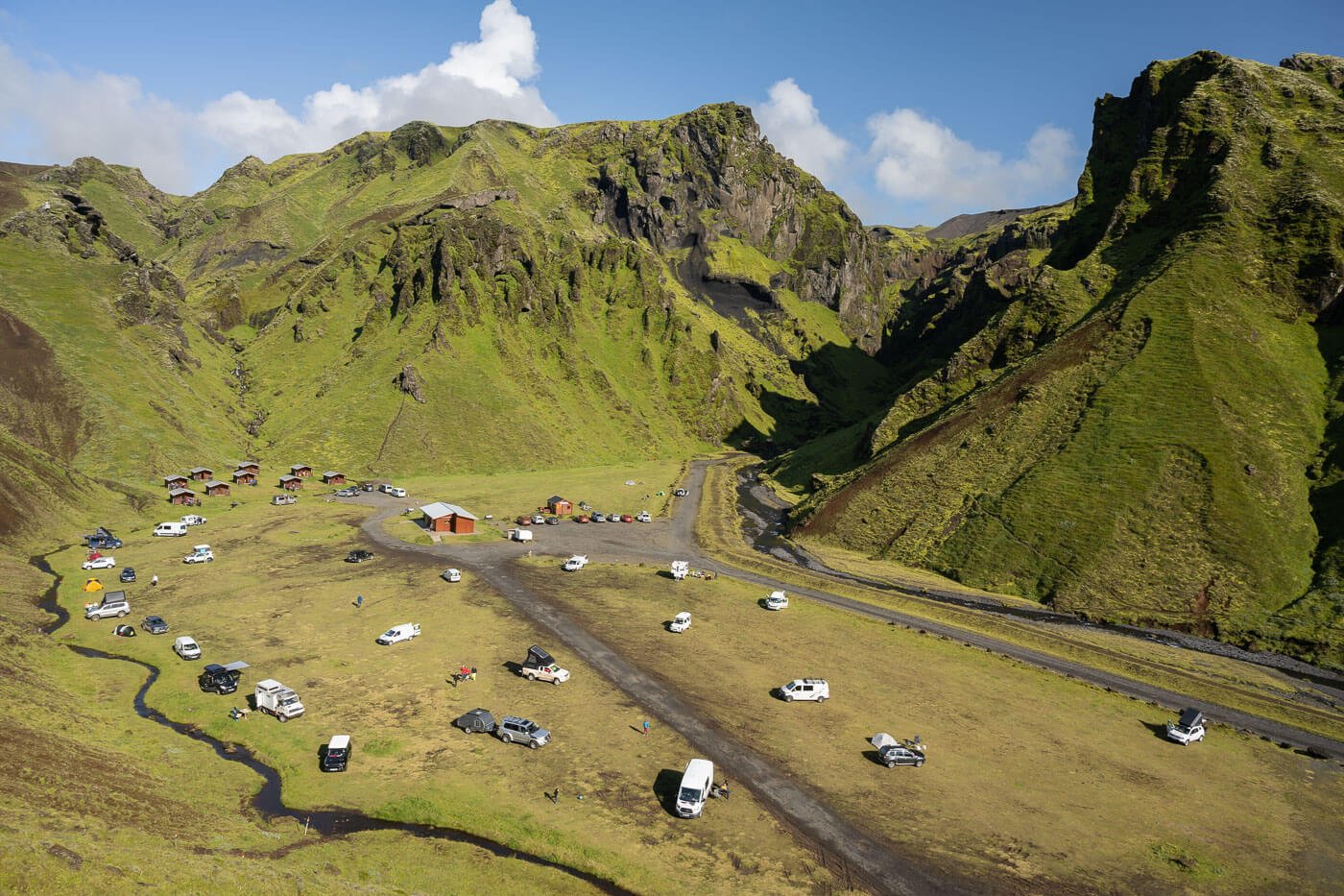 View of the Þakgil campsite from above on a sunny day, with several people camping on the grassy field.