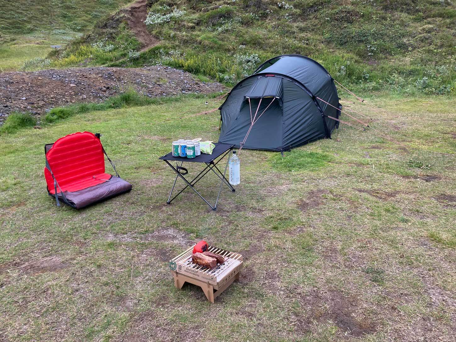 Overview of a camping setup in Þakgil with tent, chair, camping table and disposable grill.