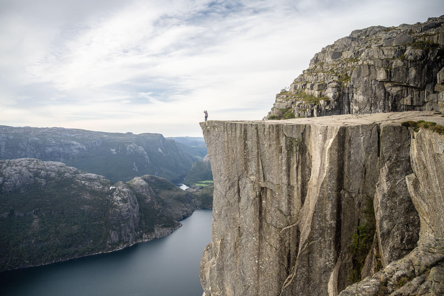 Hiker on top of the Pulpit Rock waving a hand.
