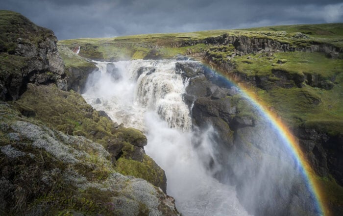 Lambhagafoss, a hidden waterfall in Iceland surrounded by green moss with a rainbow in front of it.