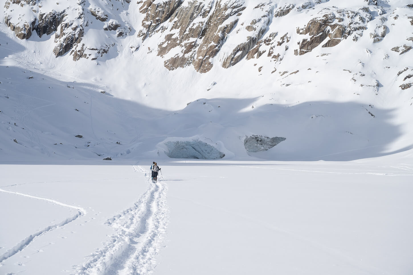 Cross-country skiers on aflat area surrounded by snowy mountains.