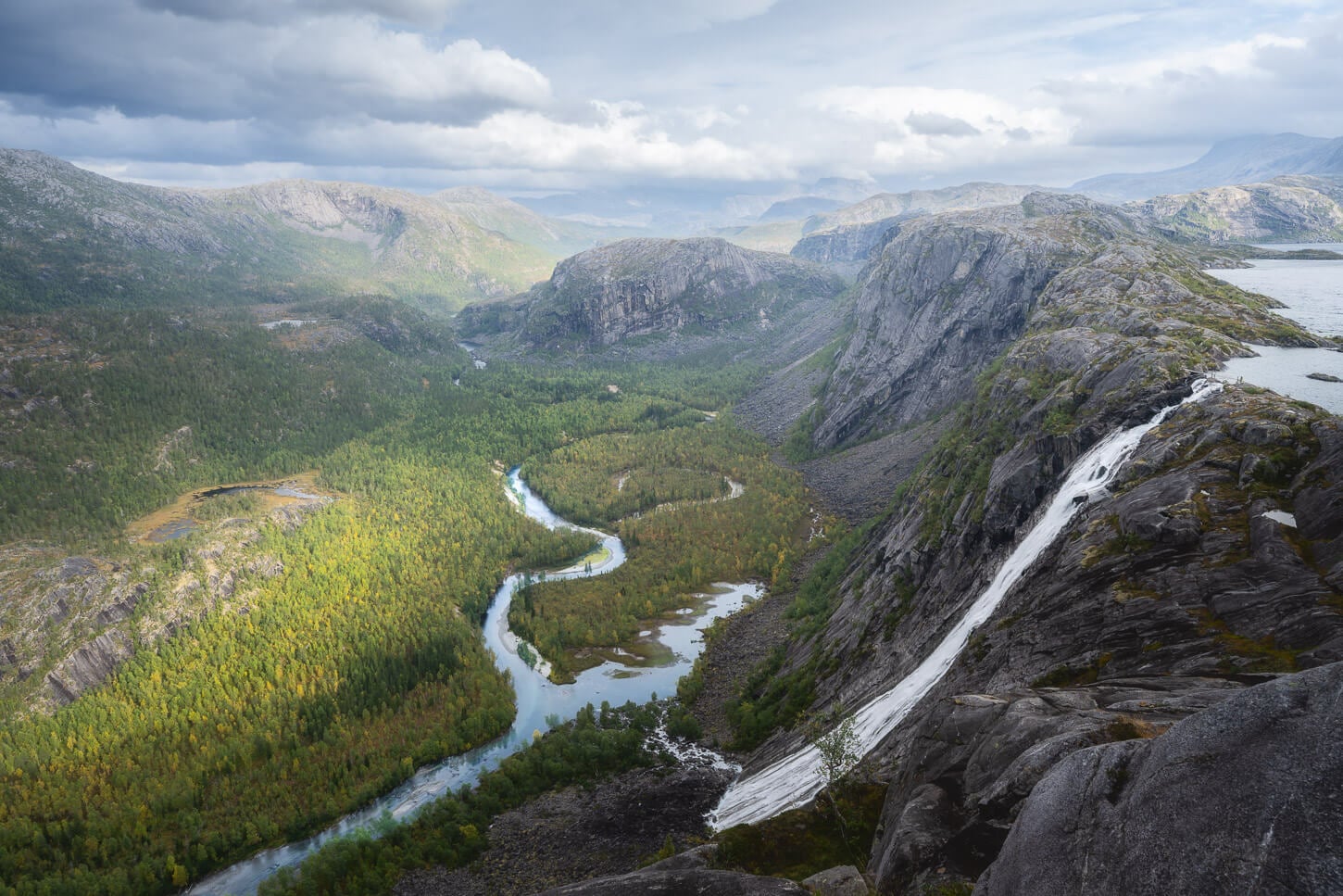 Litlverivassforsen Waterfall under a partly cloudy sky one afternoon in September, where the trees in the valley show a hint of yellow autumn color.