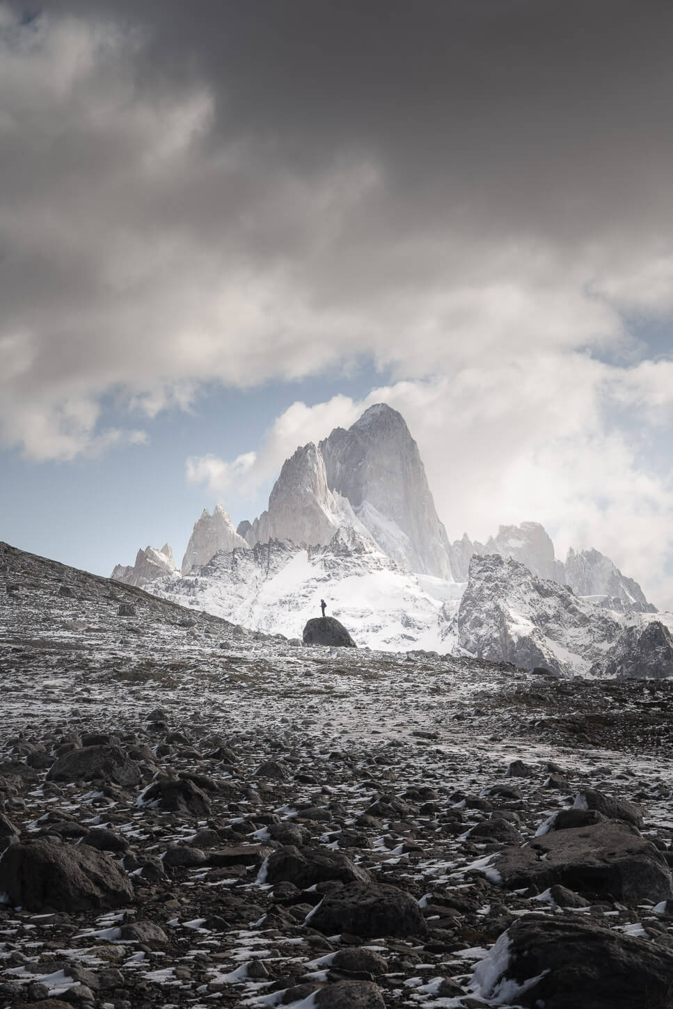 A hiker standing on a stone with the Fitz Roy. Mountain in the background.