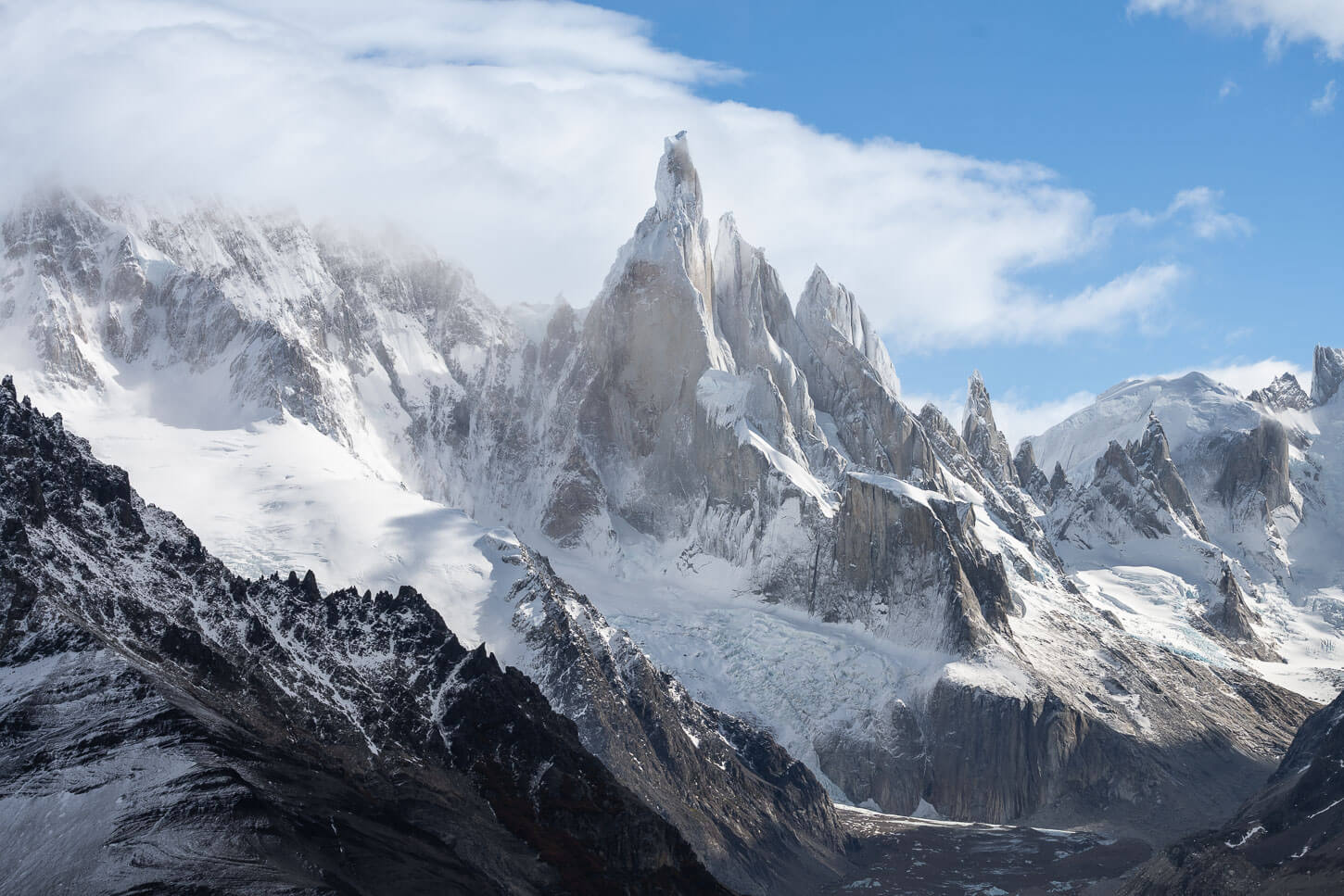 Cerro Torre is lit by the sun and partly shrouded in clouds.