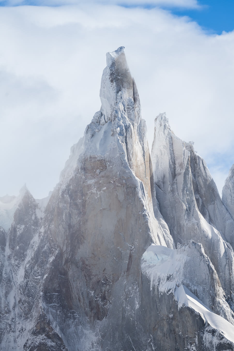 Close up image of Mount Cerro Torre under the light of an autumn sun, partly shrouded in clouds.