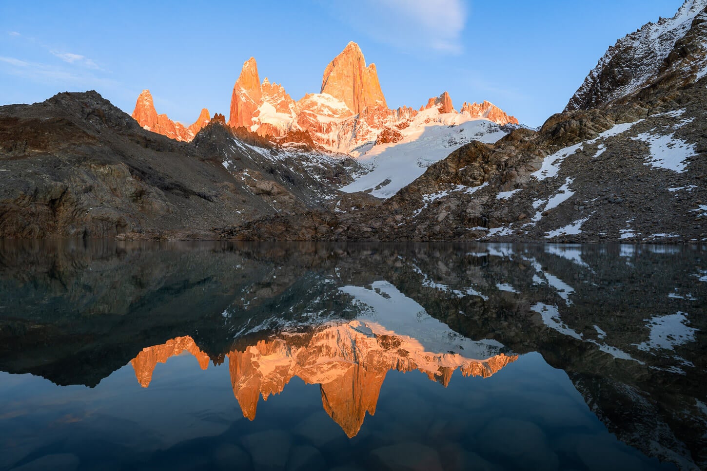 Fitz Roy and Laguna de los tres at sunrise, reflecting in the lake, at the end of the hiking trail after, withv the mountains colored in the warm light of the rising sun.