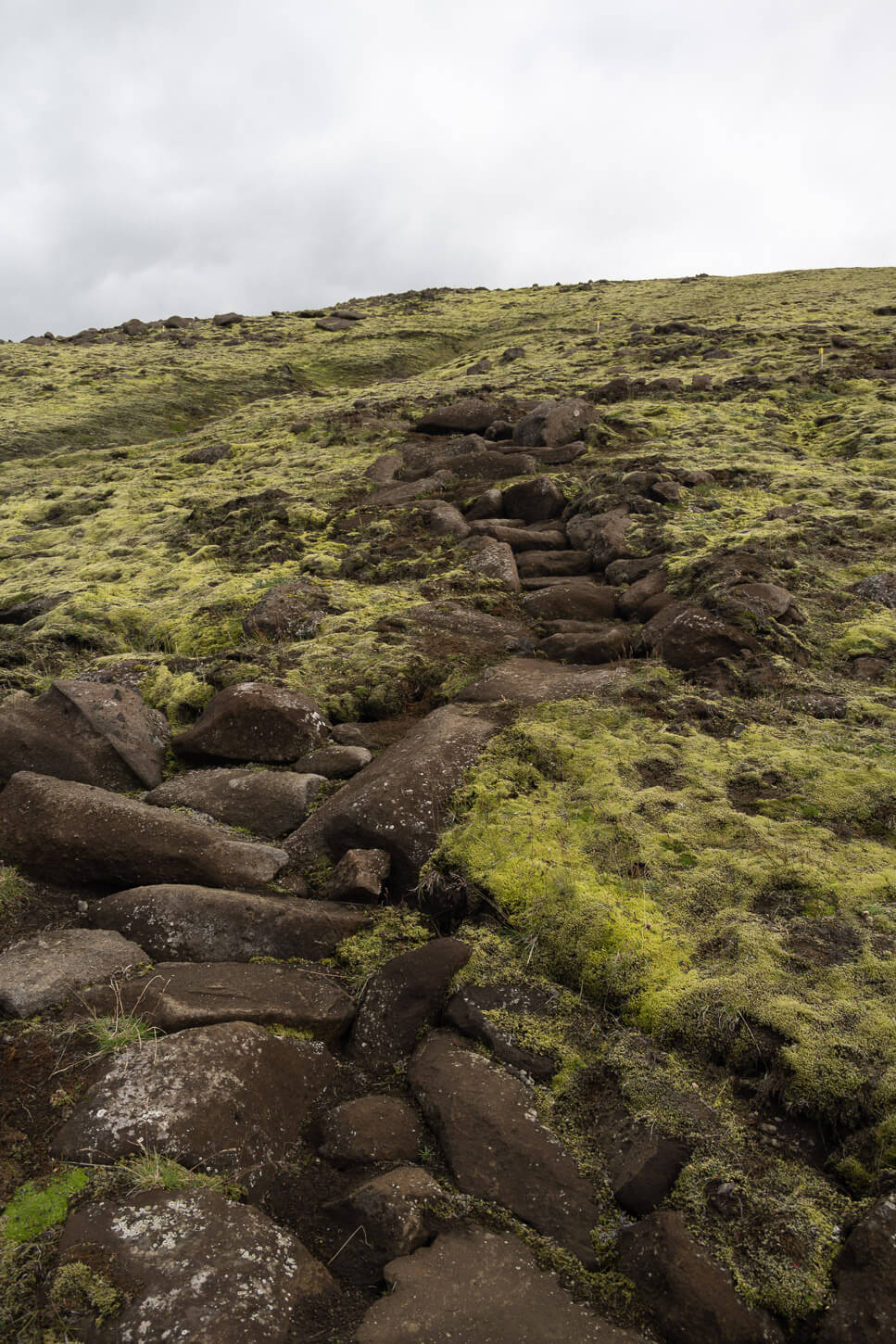 Hiking trail across a moss-covered rock fields to the top of a mountain in the highlands of iceland.
