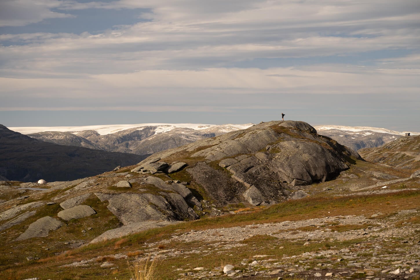 Hiker enjoying the Panorama on top of a rocky outcrop, with glaciers in the background.