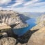 Viewpoint of Trolltunga at the end of the hike, with an hiker standing on the rock ablove the blue waters of the lake