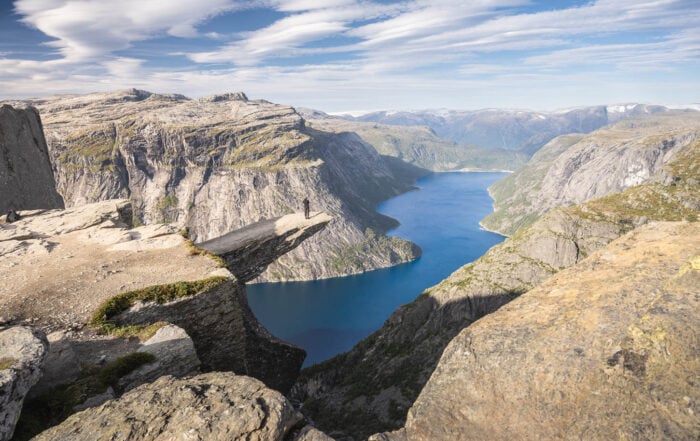 Viewpoint of Trolltunga at the end of the hike, with an hiker standing on the rock ablove the blue waters of the lake