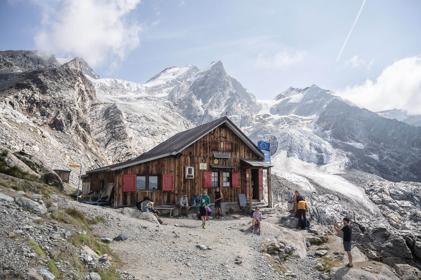 Rifugio Mezzalama on a bright sunny day, the arrival of a long hike in Val d'Ayas, with people outside the hut and glaciers perched on the mountains in the background.