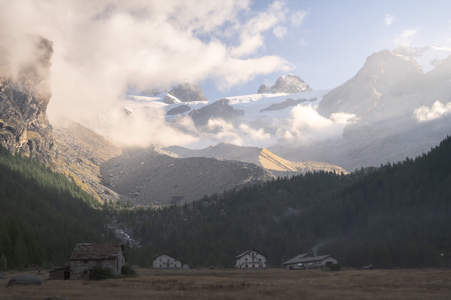 View of the houses at Piani di Verra inferiore on the hike to Rifugio Mezzalama, in the shadows of the mountain with the early morning light already warming up the glaciers and mountain peaks behind