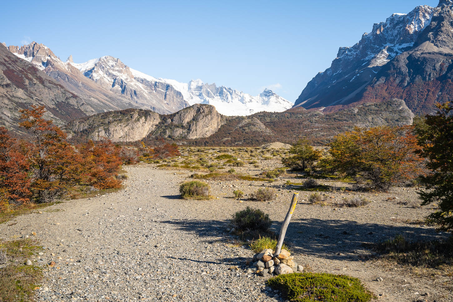 section of the mirador Piedras Blancas Hiking trail, with a trail post on the ground bushes in vibrant autumn colors on the sides, and mountain in the background.