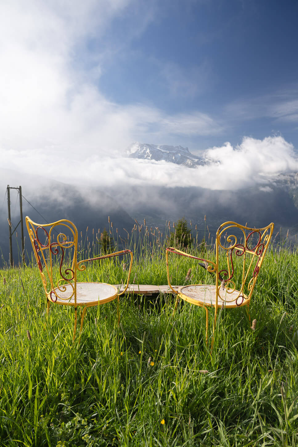 Two yello chairs on a green grassy field under a deep blue sky in Belalp, overlooking the upper rhone valley