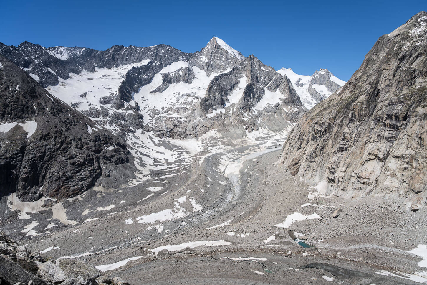 Glaciers merging in a valley with towering, steep rocky mountain.
