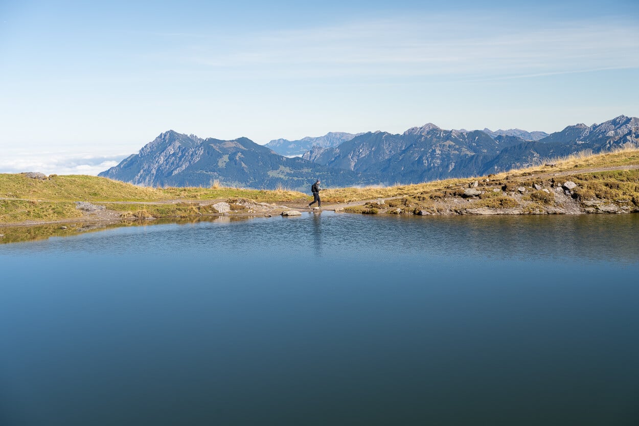 Hiker passing by the Baschalvasee lake on the Pizol five lakes hike, under a clear blue sky.