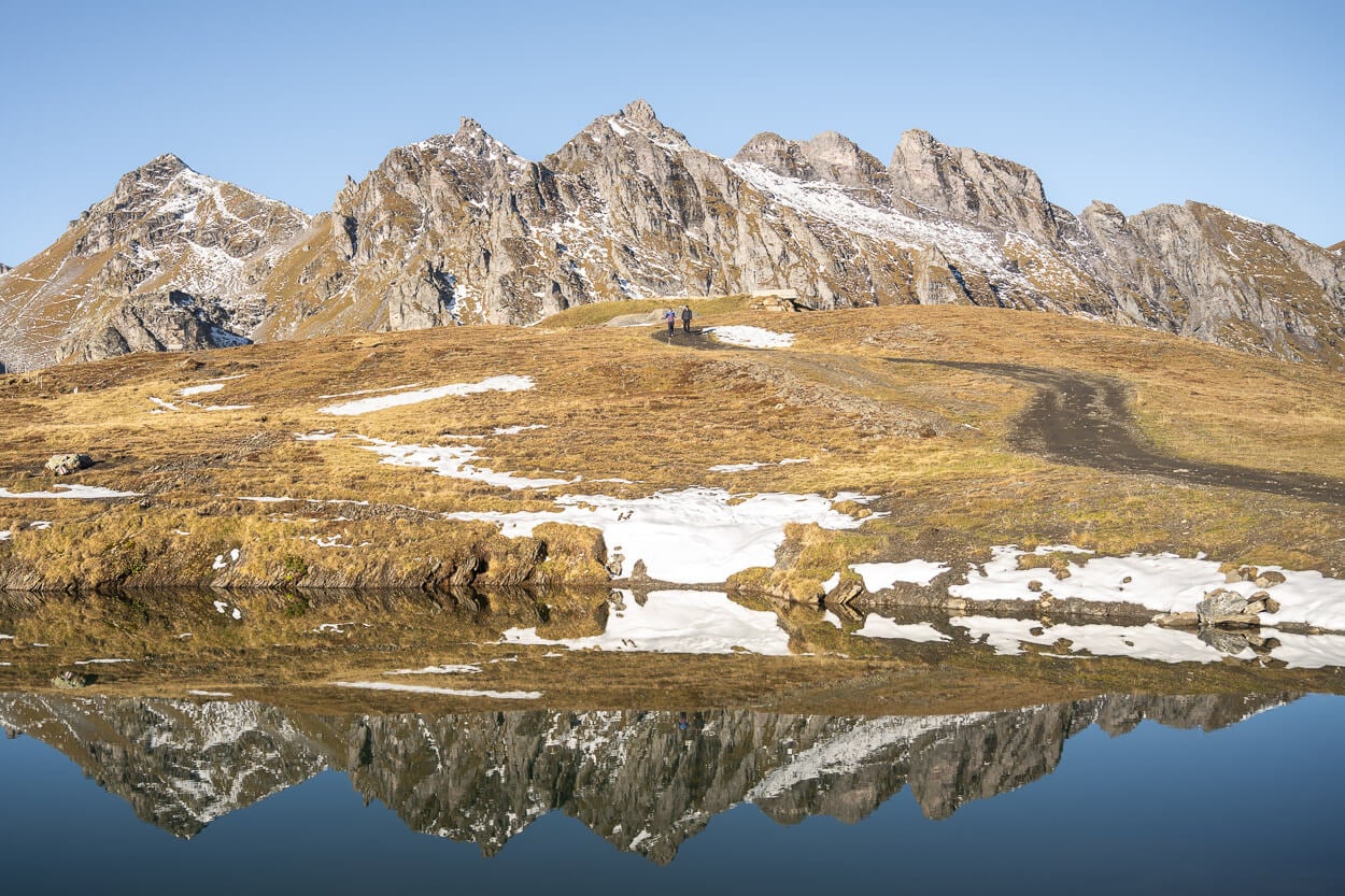 Hikers on the pizol five lakes trail, with mountains in the backdoung and a lake where the whole scene is reflected