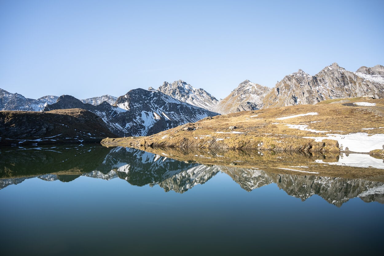mountains reflecting into the calm waters of Wangsersee, on an autumn day with clear skies, and some snow on the ground already.