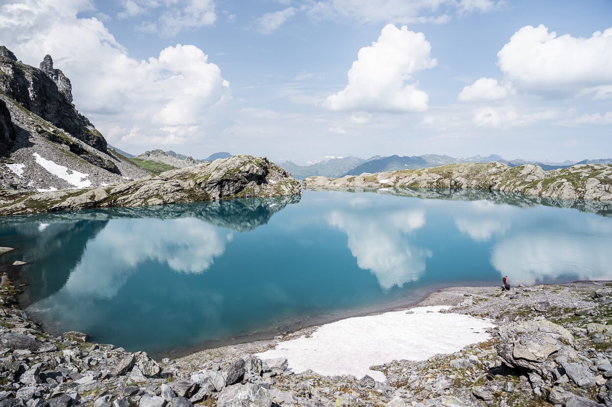 rocky shores of Schottensee on the Pizol five lakes hike, with clouds reflecting in the turqoise waters of the lake surrounded by rocks